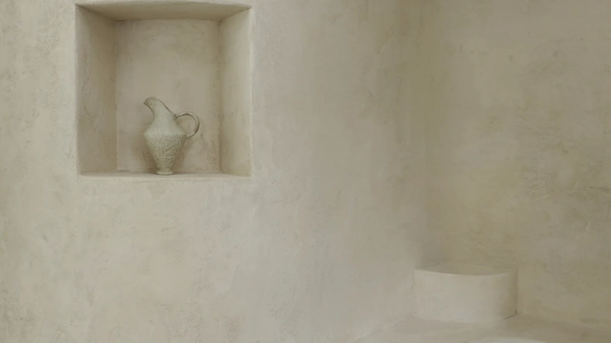 A plaster niche with a single vase in soft afternoon light at Soom