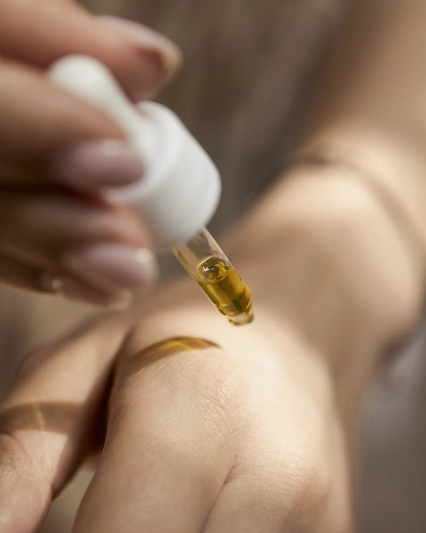 A drop of serum resting on the back of a hand in warm window light
